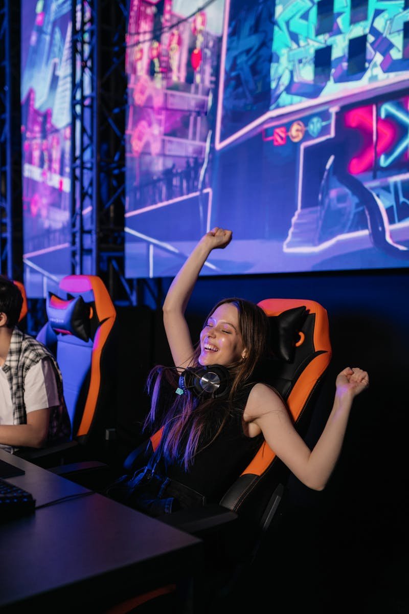 Young woman celebrating victory in neon-lit gaming room with headset.