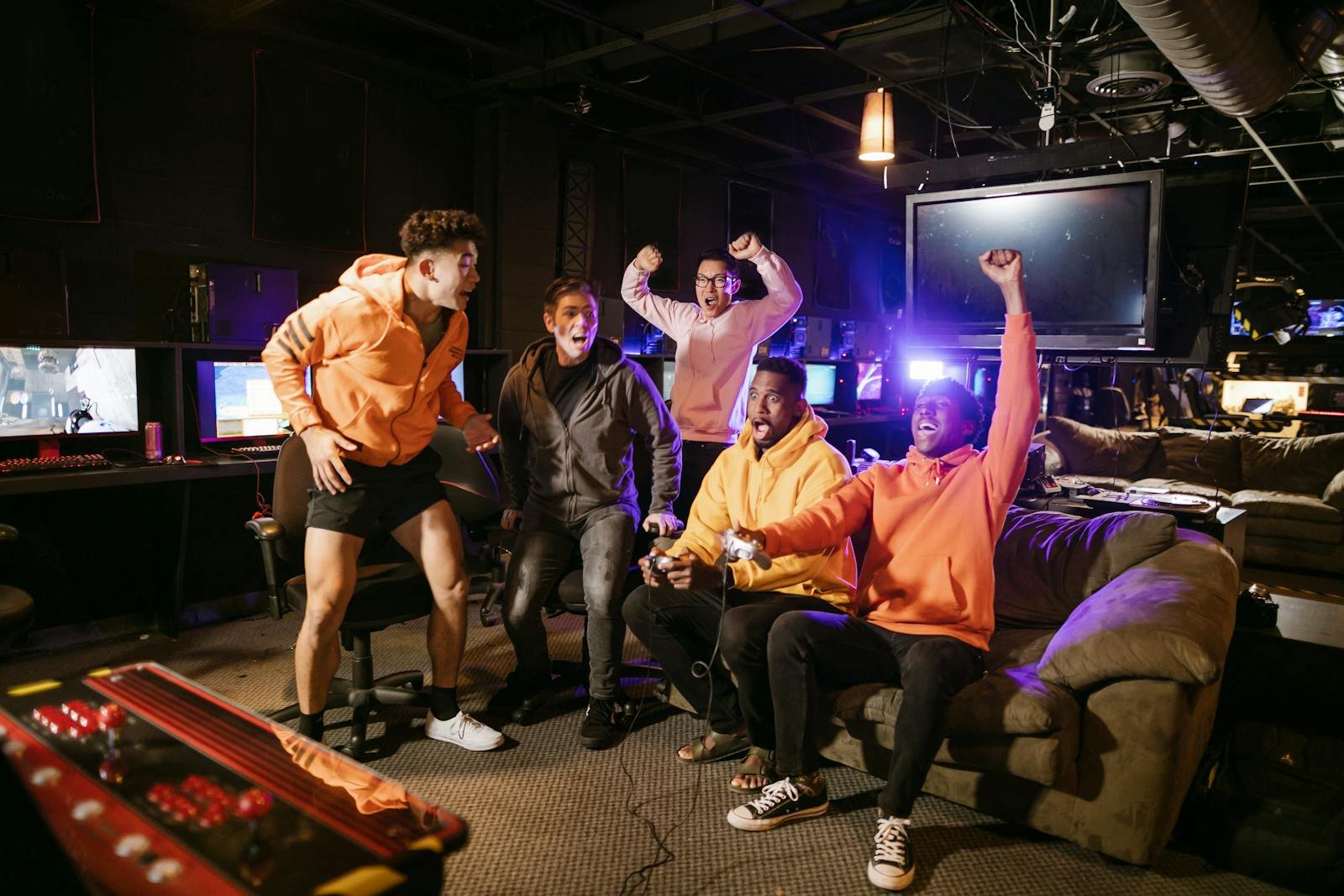 Five diverse friends celebrating a gaming victory indoors, showcasing teamwork and joy.